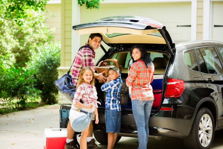 Happy family of four packing their car for a vacation trip